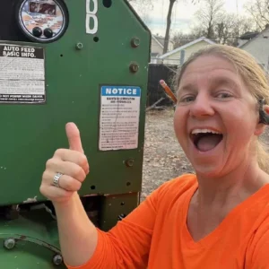 Woman thumbs-up, happy, by green machine.